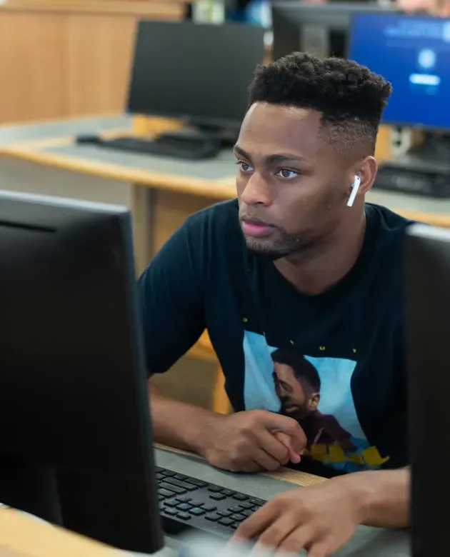 A student sits at a computer in the Biddeford Campus library